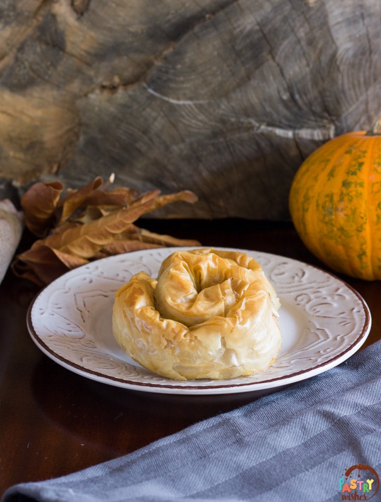 Greek pumpkin hand pie on a plate with pumpkin, leaves and kitchen towel