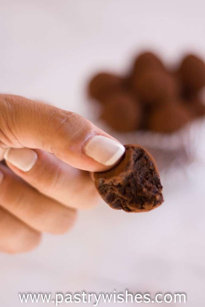 a hand holding a vegan chocolate truffle with other truffless in a glass bowl in the background