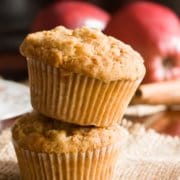 two streusel top apple mufins, one on top of the other, with two apples and cinnamon sticks