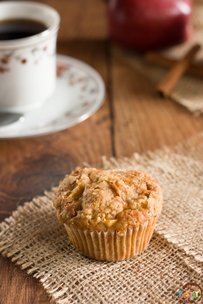streusel topappl muffin on a table with coffe, an apple and cinnamon sticks