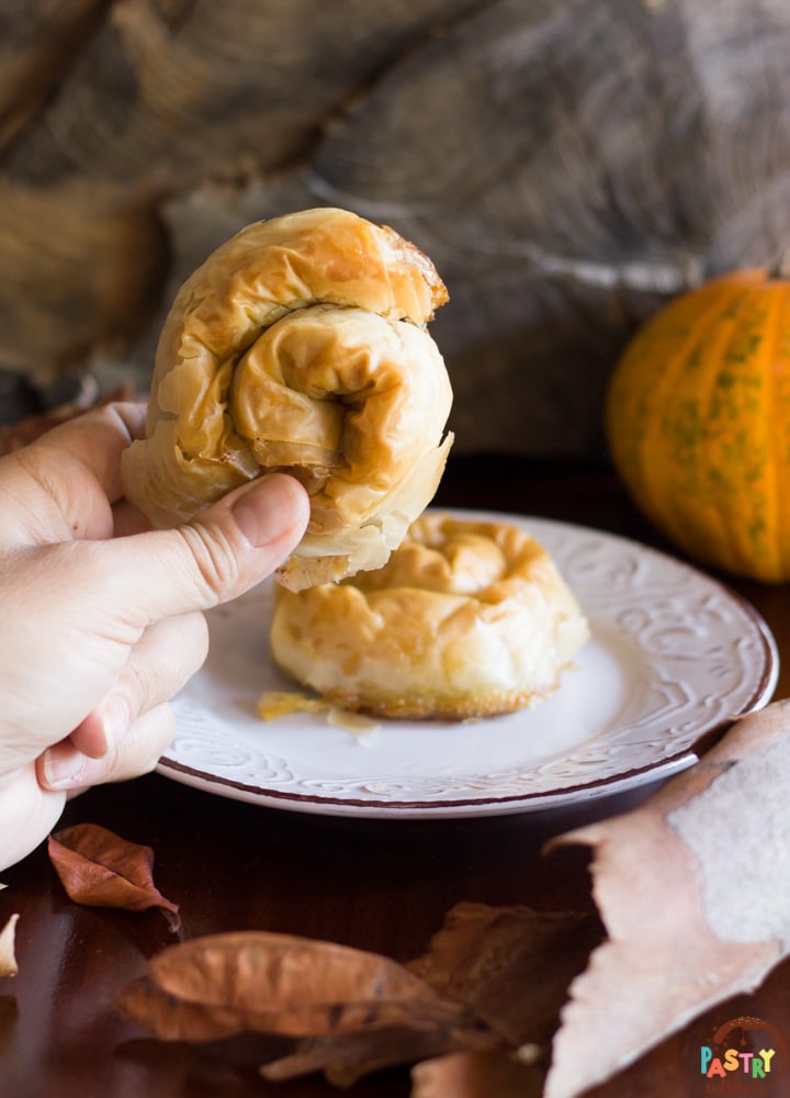 greek pumpkin hand pies, one on a plate and one in a hand with pumpkin and leaves