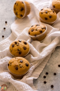Vegan Chocolate Chip Muffins on a white towel with some chocolate chips on the countertop