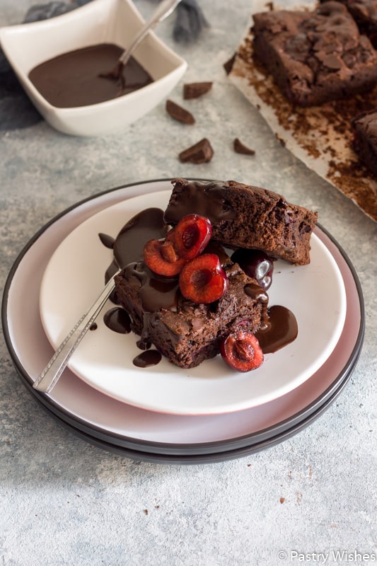 3 pieces of chocolate cherry brownies on a plate with fresh cherries and chocolate syrup