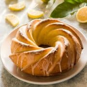 lemon olive oil cake on a white plate with lemon slices and branch in the background