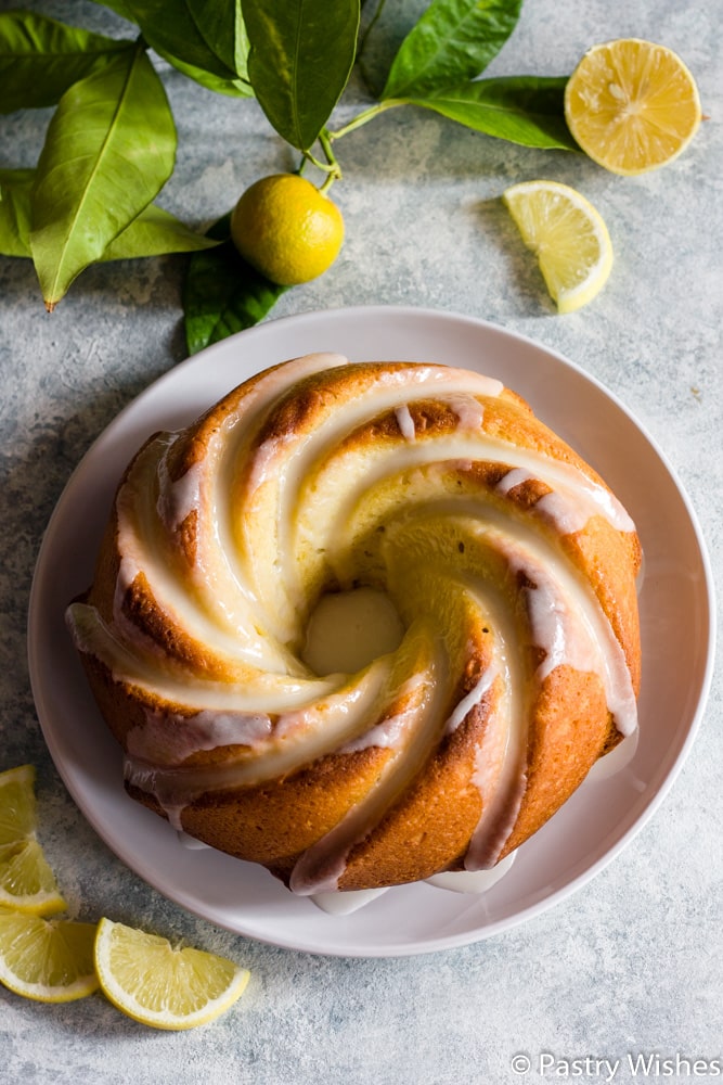 lemon olive oil cake on a white plate with lemon slices and branch in the background