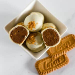 Biscoff truffles in a white bowl with lotus cookies on a white surface.
