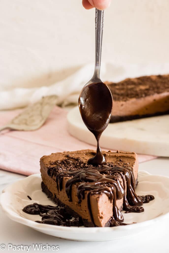 drizzling chocolate sauce on a slice of eggless chocolate cheesecake
