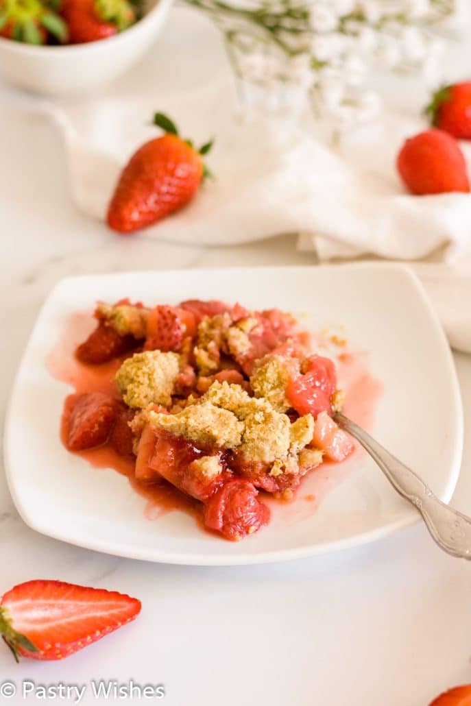 strawberry and apple crumble on a white plate with strawberries in the background