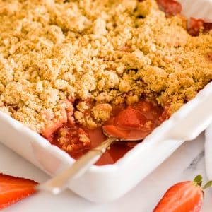 A close up of strawberry and apple crumble in a white baking dish.