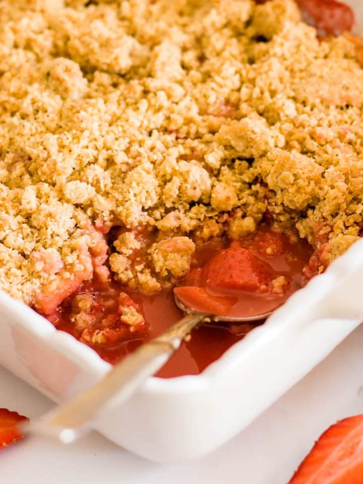 A close up of strawberry and apple crumble in a white baking dish.