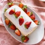 A vanilla swiss roll cake with powdered sugar and fresh strawberries on a white plate.