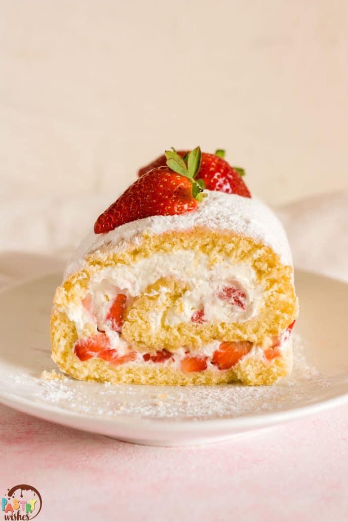a close up of vanilla swiss roll cake with powdered sugar and fresh strawberries on a white plate