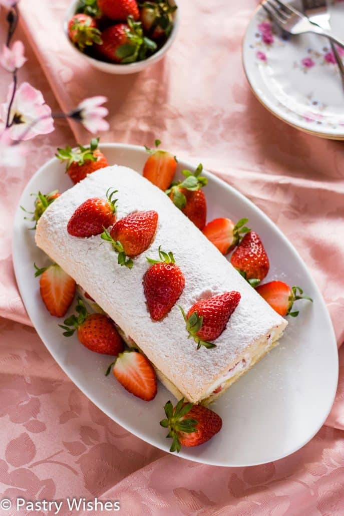 vanilla swiss roll cake with powdered sugar and fresh strawberries on a white plate