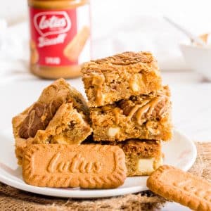 Biscoff blondies on a white plate with biscoff cookies and biscoff spread in the background.