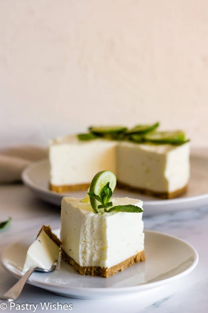 a slice of cheesecake on a white plate with a slice of lime and a sprig of mint