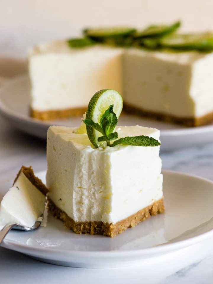 A slice of mojito cheesecake on a white plate with cut cheesecake in the background.