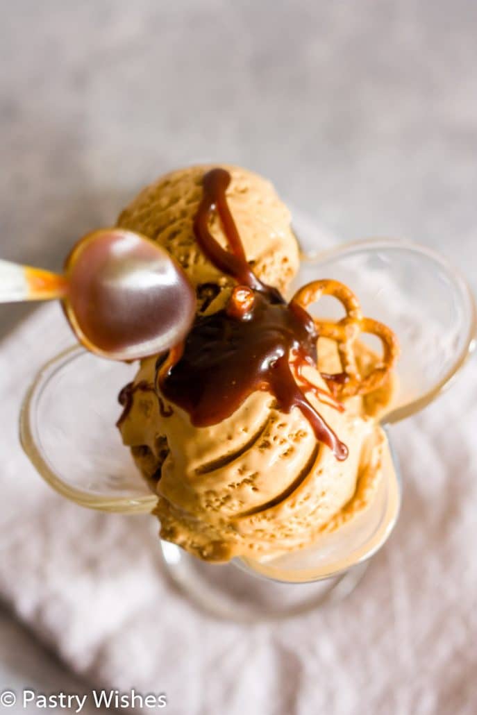 salted caramel pretzel ice cream in a glass with a spoon drizzling caramel on top