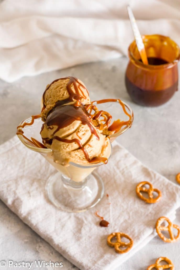 salted caramel pretzel ice cream in a glass with a jar of caramel in the background
