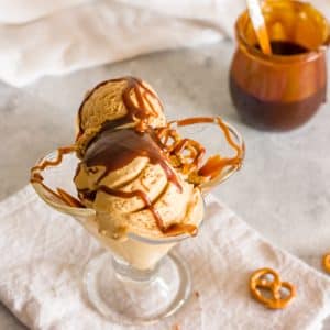 Salted caramel pretzel ice cream in a glass with a jar of caramel in the background.