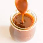 Salted caramel sauce dripping from a spoon into a jar.
