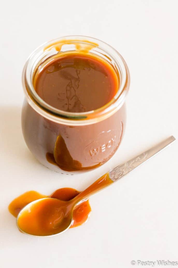 salted caramel sauce in a jar with a spoon full of caramel sauce on white surface