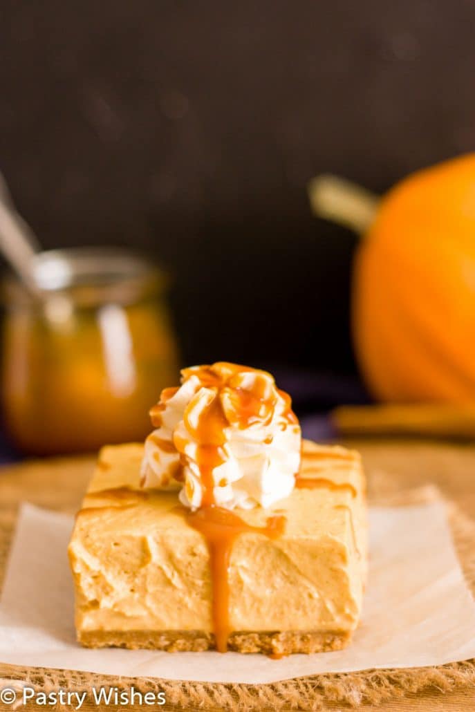 a slice of pumpkin cheesecake bar with whipped cream and caramel sauce on top and pumpkin in back