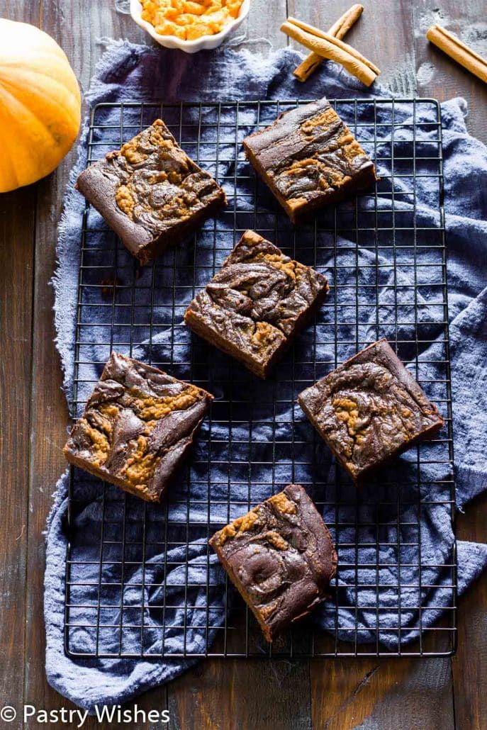 overhead shot of vegan pumpkin brownies on a wire rack with a pumpkin and cinnamon sticks in the background