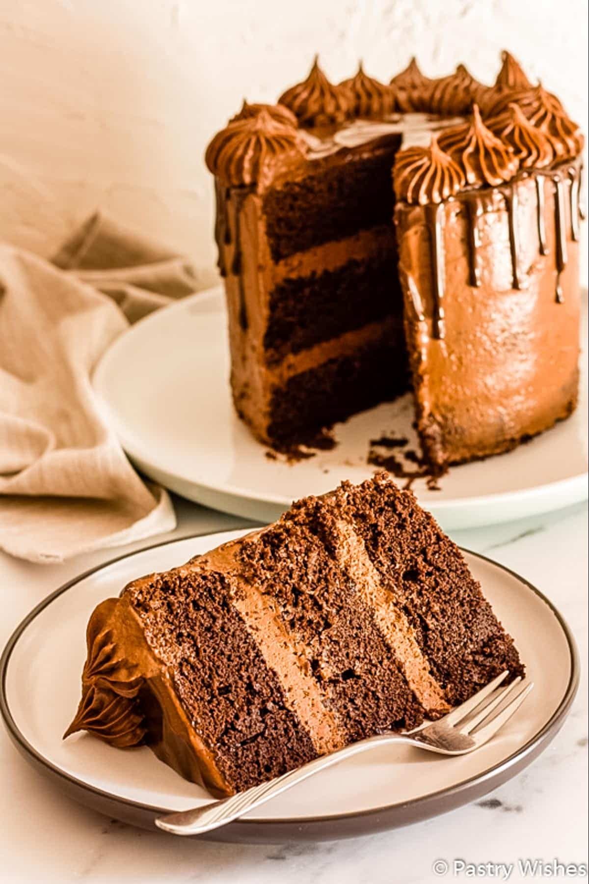 A slice of a 3 layer chocolate drip cake on a plate.