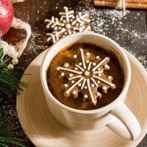 A gingerbread mug cake with gingerbread cookies on a wooden surface with Christmas decorations and powdered sugar.