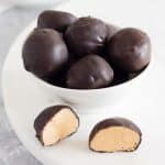 Peanut butter balls in a white bowl on a white surface.
