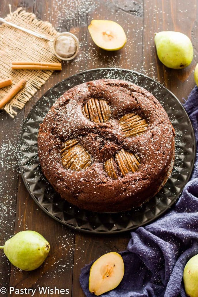 An overhead shot of a pear and chocolate cake on a black plate and wooden surface.