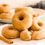 A stack of cinnamon sugar donuts on parchment paper next to a cinnamon stick.