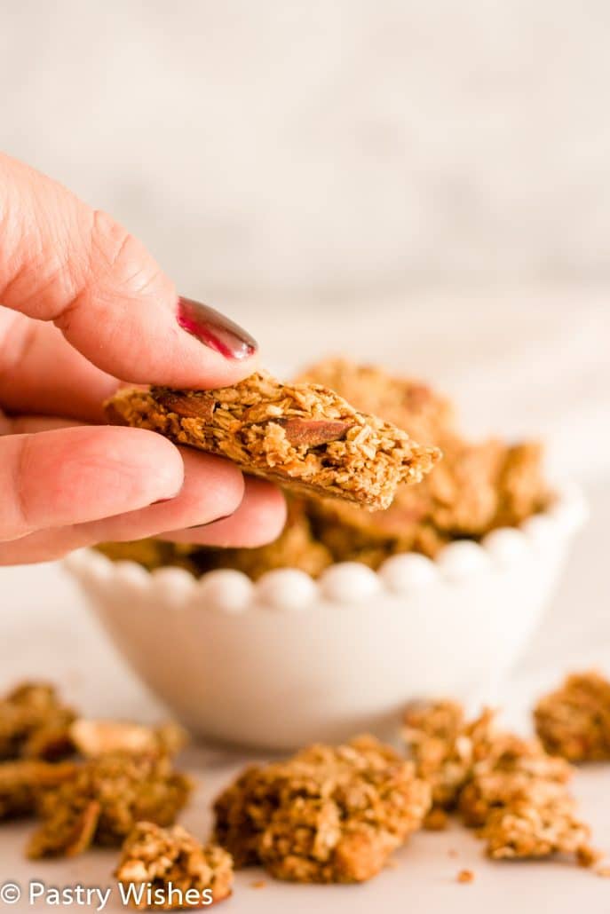 A close up of a hand holding a piece of homemade granola clusters.