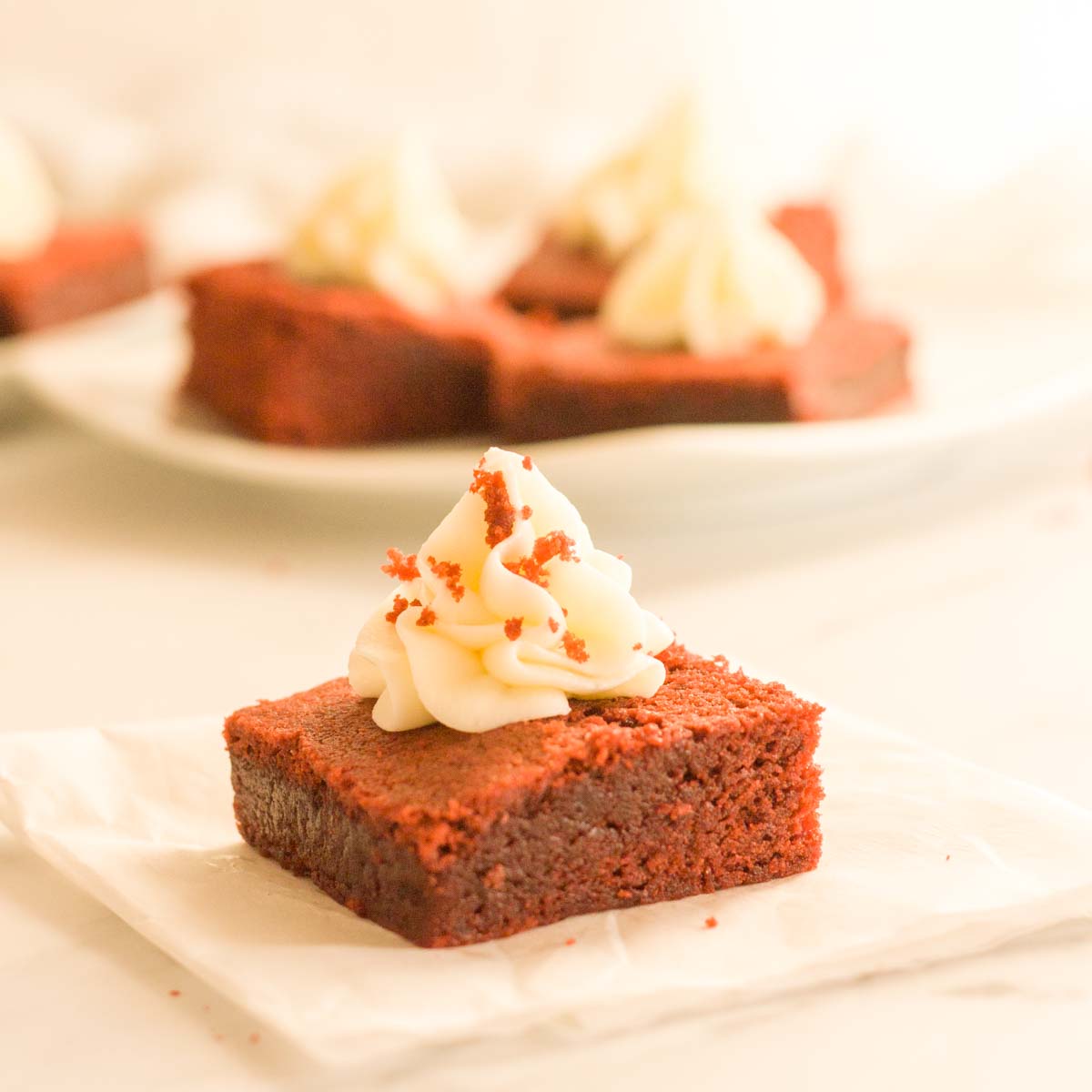 A close up of a red velvet brownie topped with cream cheese frosting on parchment paper.
