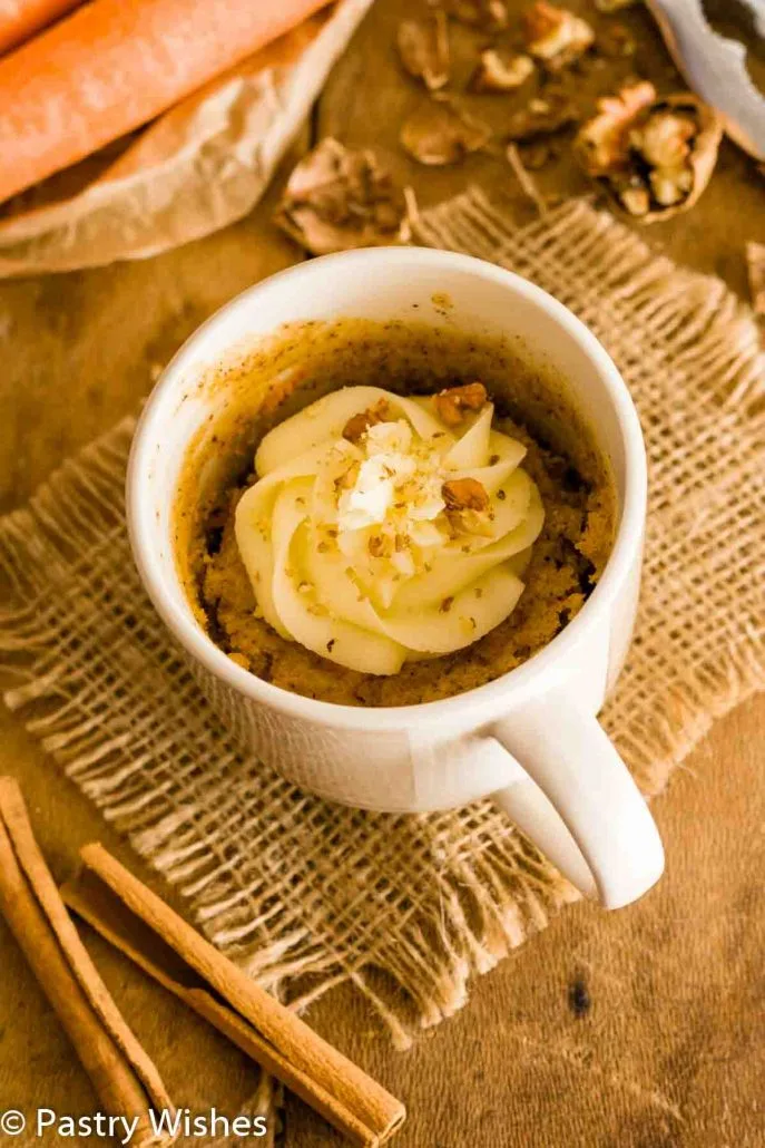 A carrot mug cake topped with cream cheese frosting and chopped walnuts.