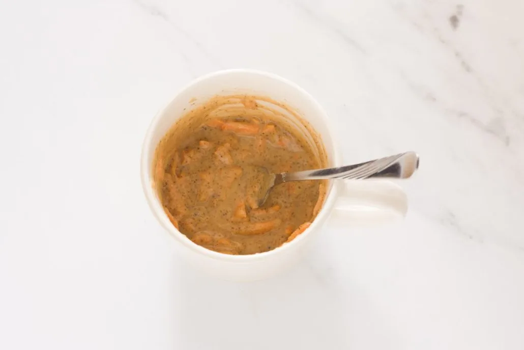 Stirring ingredients for carrot mug cake with a fork.
