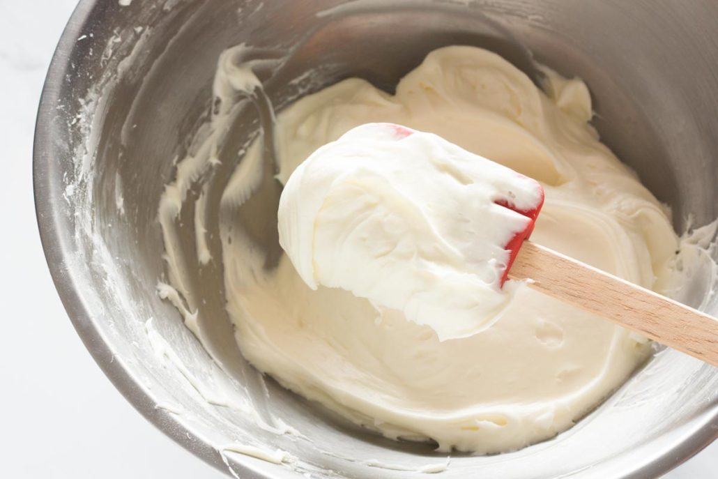 Close up of cream cheese frosting on a spatula over a mixing bowl.