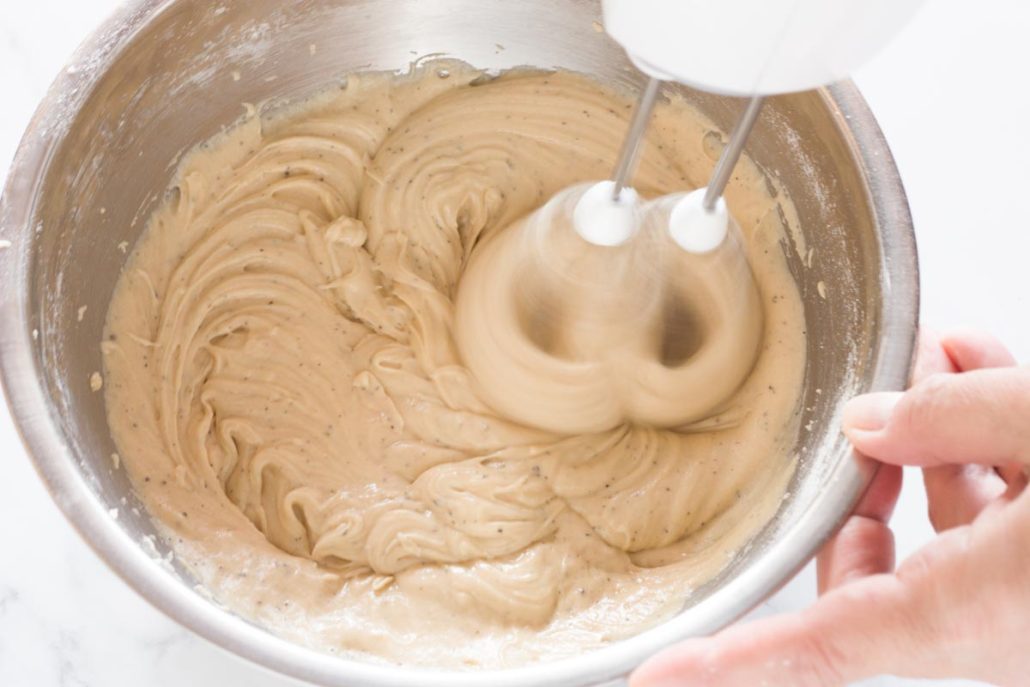 Beating flour mixture with wet ingredients using a hand mixer.