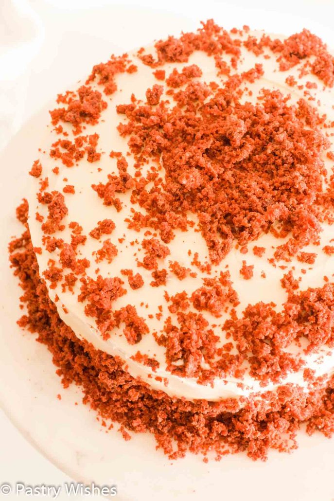 An overhead shot of eggless red velvet cake topped with cream cheese frosting and red cake crumbs.