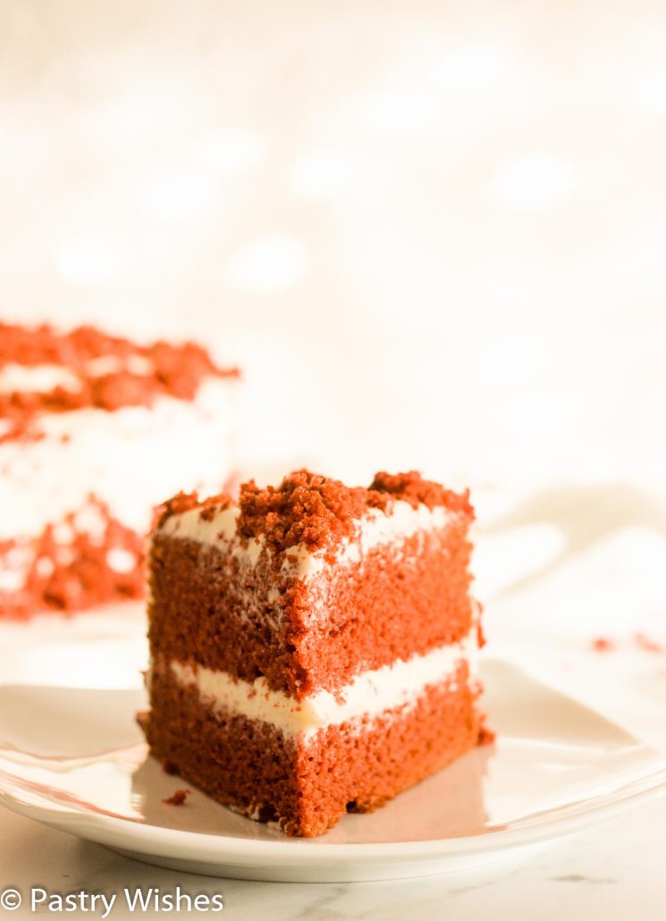 A close up of a slice of eggless red velvet cake with cream cheese frosting.
