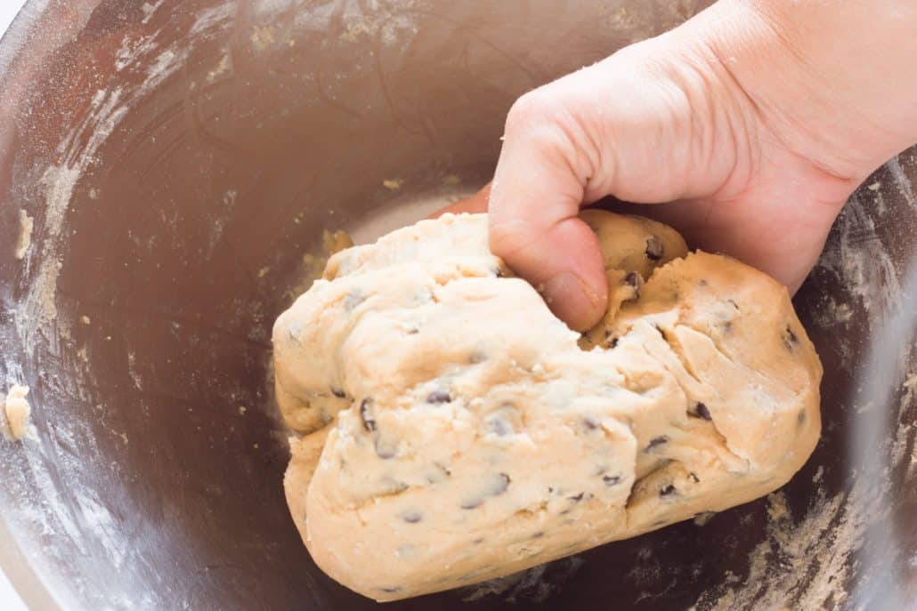 Holding chocolate chip cookie dough in one hand.