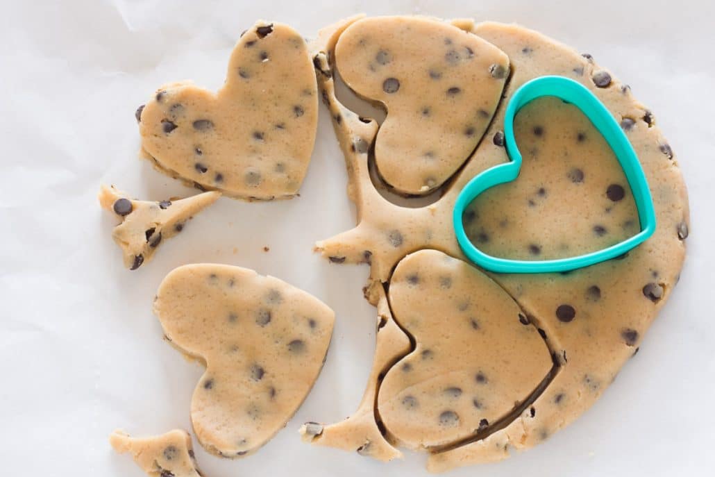 Cutting out chocolate chip cookie dough with a heart shaped cookie cutter.