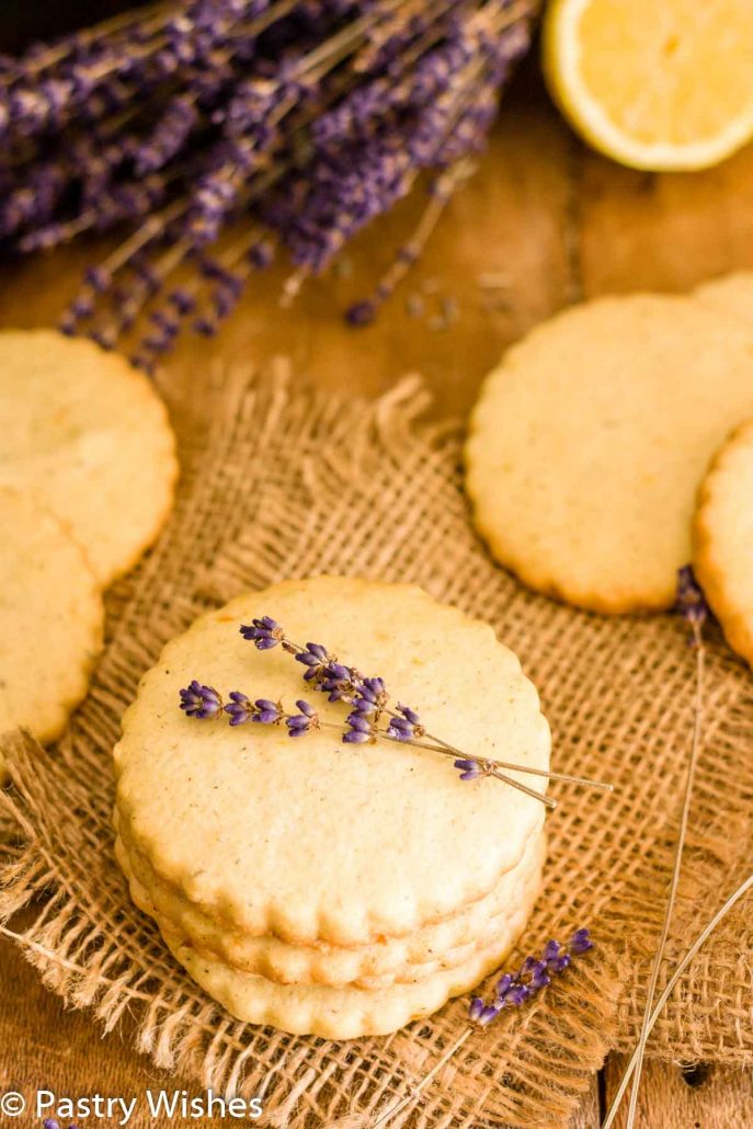 Lemon lavender cookies on a wooden table with lavender flowers and lemon in background.