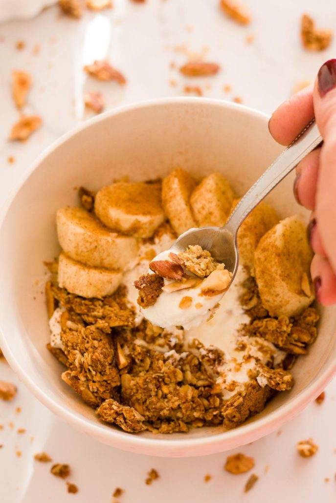 A close up of a hand holding a spoon filled with Greek yogurt with granola.