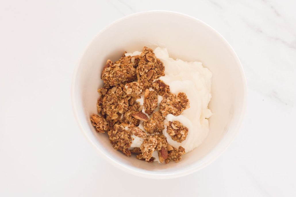 A white bowl filled with Greek yogurt and topped with homemade granola clusters.