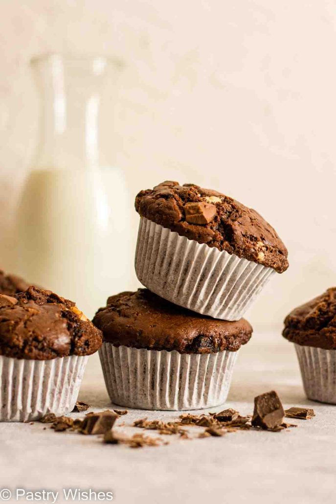 Triple chocolate muffins next to milk and chunks of chocolate on a gray surface.