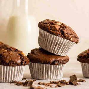 Triple chocolate muffins next to milk and chunks of chocolate on a gray surface.