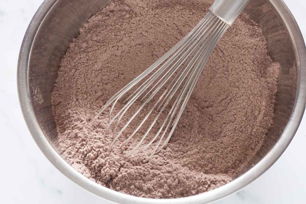 Whisking flour, cocoa powder and other dry ingredients in a large mixing bowl.