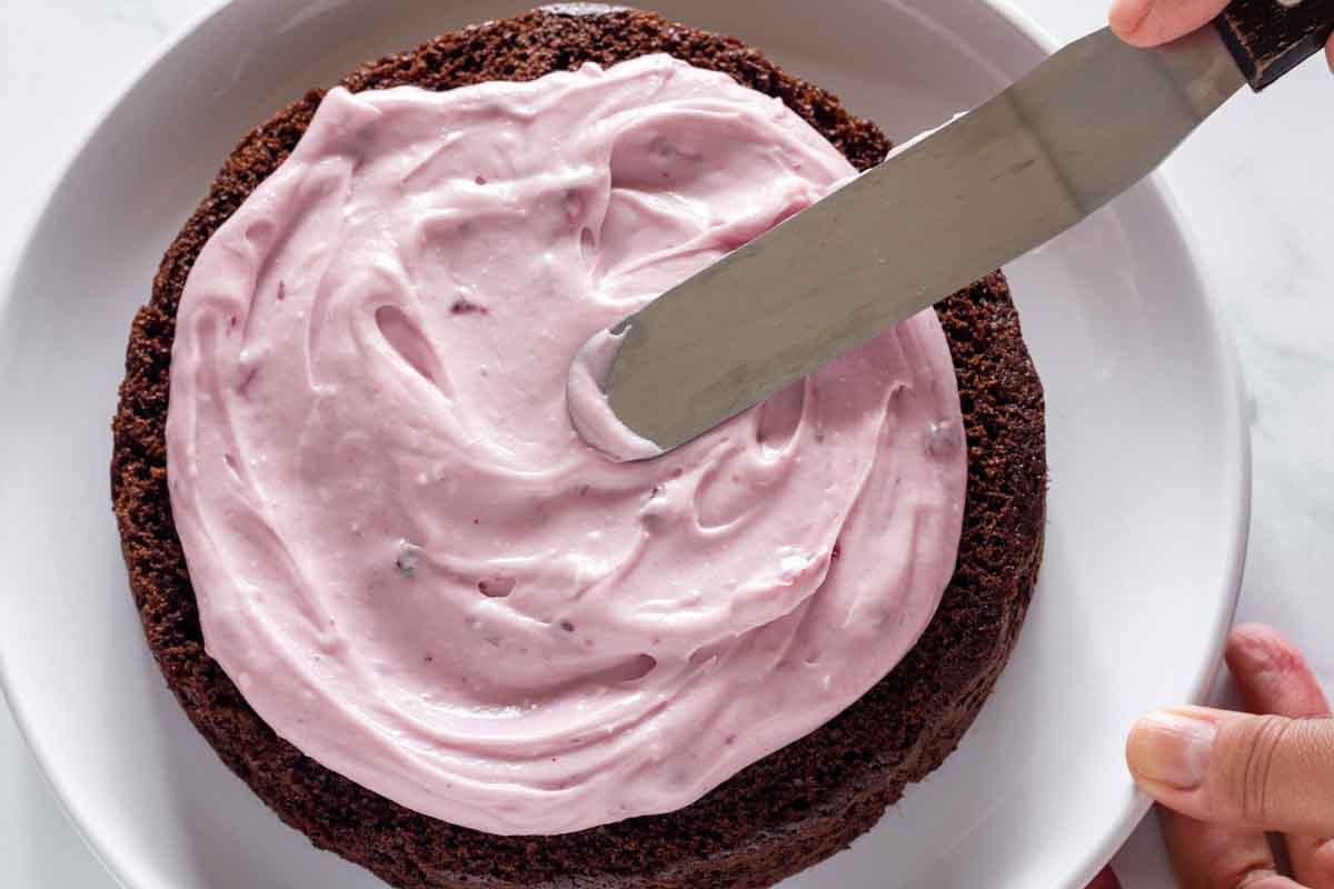 Spreading blueberry cream cheese frosting on a chocolate cake layer with an offset spatula.