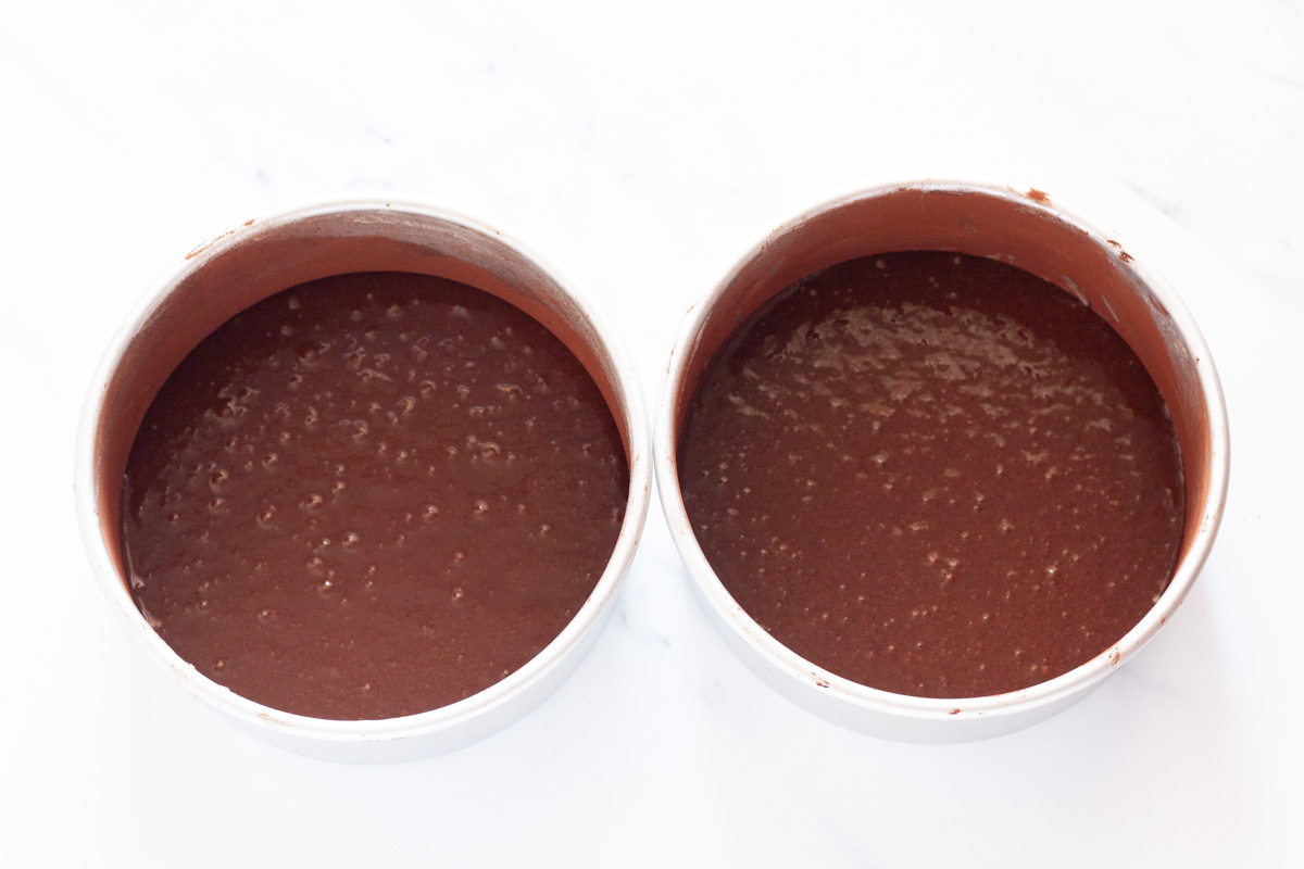 Two cake pans filled with chocolate cake batter.